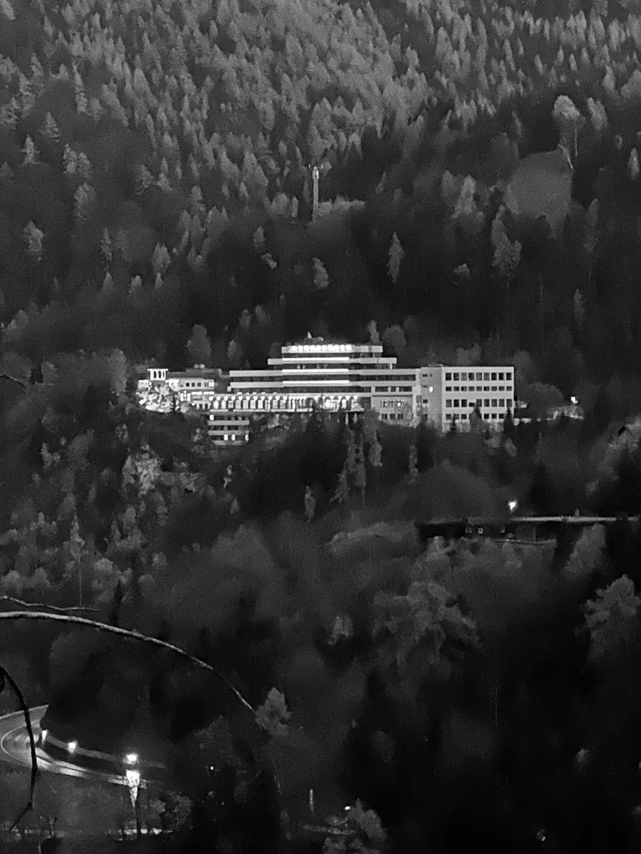 The lit hotel seen from the mountain at night, forest all around