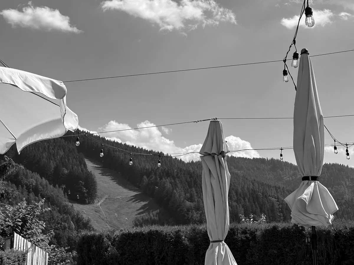 The Cervo d’Oro terrace in summer, umbrellas closed, string lights overhead, the slopes behind